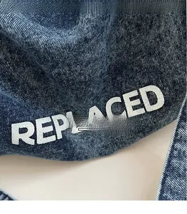 Close-up of dark wash denim fabric texture with white REPLACED printed lettering detail