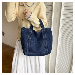 Detailed view of a dark blue denim tote bag with contrast stitching and front pocket