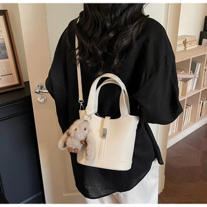 Detalle del bolso de cubo en cuero granulado blanco con hebilla de metal y colgante
