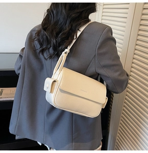 Detail view of ivory pebbled leather shoulder bag with functional side pocket on gray suit
