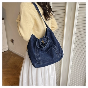 Detail of deep blue denim tote bag with contrast stitching and shoulder strap on model