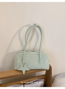 Detail of mint green leather baguette bag with star charm on a wooden magazine rack