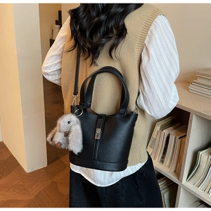 Detalle de bolso cubo de cuero negro con cierre metálico y adorno de conejo de peluche