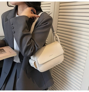 Model wearing a minimalist cream leather shoulder bag with sleek flap and metal buckle detail