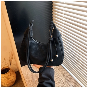Detail of black suede crescent bag featuring knotted strap and silver orb ornaments