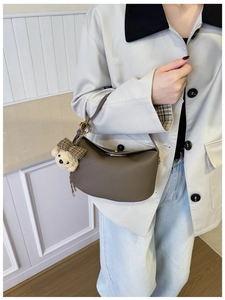 Detail of dark brown leather crescent handbag with cute white bear plush charm on side