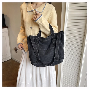 Detail of a casual black denim tote bag with visible stitching and outer pocket for daily use