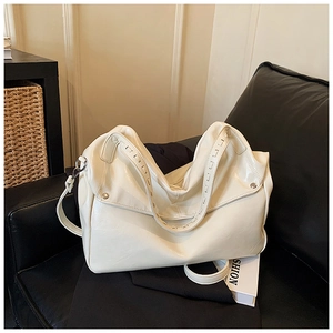 Dettaglio dell'elegante borsa tote in vernice bianco crema su divano in pelle nera