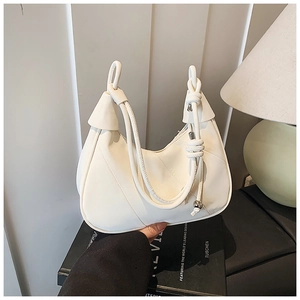 Detail of creamy white crescent handbag with leather knot handle and silver ball charm