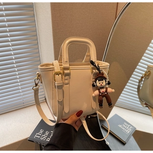 Détail du mini sac seau crème avec doubles poignées et un pendentif de dessin animé mignon