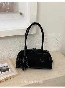 Detail of black suede shoulder bag featuring white contrast stitching and a star charm