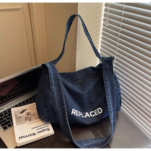 Detail view of large denim tote bag with white REPLACED lettering in casual office setting