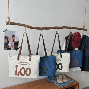 Detailed close-up of large canvas tote bag hanging on wooden branch with Loo graphic print