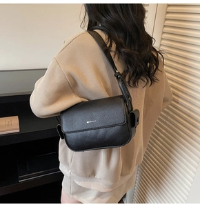 Detail view of black lychee grain leather crossbody bag styled with a beige knit sweater