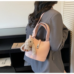 Detalle del bolso tipo cubo de cuero granulado rosa con un conejo de peluche en el asa