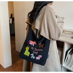 Detail view of black canvas tote bag with colorful animal patchwork embroidery on shoulder