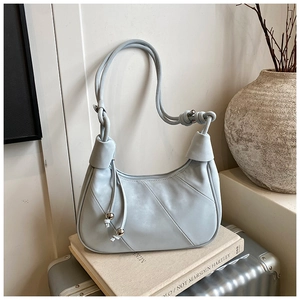 Detail of greyish-blue crescent bag with decorative knot, stitching, and tassel charm