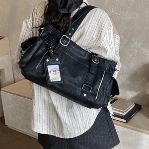 Dettaglio borsa tote in pelle nera con fibbie regolabili e ciondolo decorativo a cartone