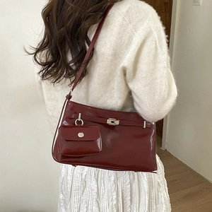 Dettaglio borsa sottobraccio in vernice rosso scuro con chiusura metallica e pochette