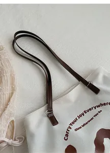 Close-up of durable white canvas tote bag with brown leather strap and slogan detail