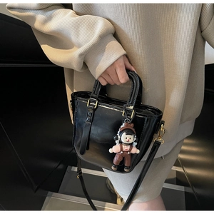 Détail d'un sac seau noir brillant avec garnitures dorées et charm de dessin animé