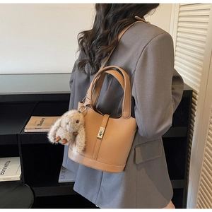 Detalle de un bolso de cubo en cuero marrón con un tierno accesorio de conejo de peluche