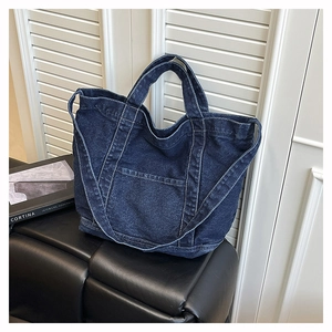 Detail of a navy blue denim tote bag with contrast stitching on a black leather stool