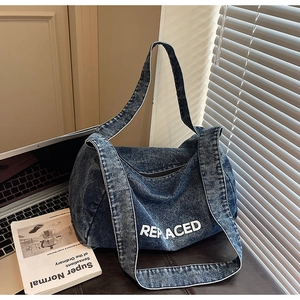 Detailed view of large blue denim tote bag with white REPLACED print in a lifestyle setting