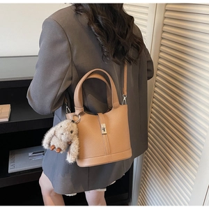 Bolso cubo de cuero marrón con un colgante de conejo gris sobre una americana gris