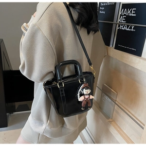 Détail du sac seau en cuir verni noir avec ferrures dorées et breloque de dessin animé