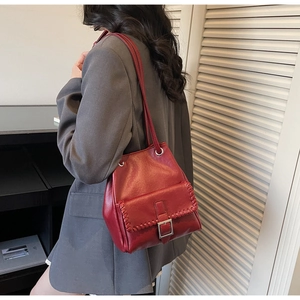 Vue détaillée du sac seau bordeaux avec bords tressés porté sur un blazer gris chic