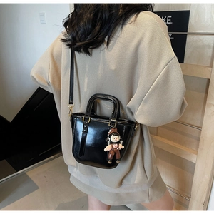 Détail d'un sac seau en cuir noir brillant avec un pendentif poupée de dessin animé mignon