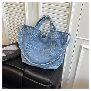 Detail of blue washed denim tote bag with sturdy stitching and front pocket on leather seat