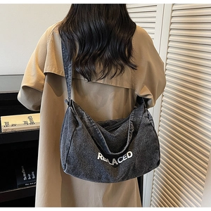 Detail view of large grey denim tote bag with REPLACED print worn over a beige trench coat