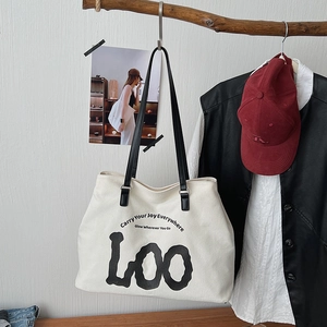 Detail of white canvas tote bag with black leather strap and artistic slogan printing