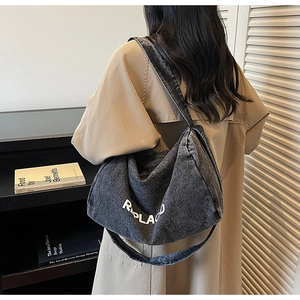 Street style view of a large grey washed denim hobo bag with white REPLACOD lettering