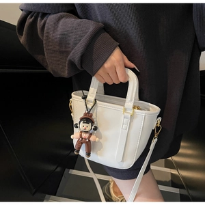 Détails d'un sac seau blanc avec ferrures dorées et pendentif de poupée mignon