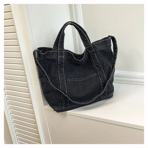 Close-up of black denim tote bag featuring white contrast stitching and outer pocket detail