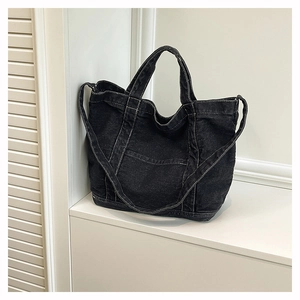 Detail of black denim tote bag with white contrast stitching and versatile shoulder strap