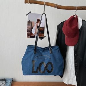 Detailed macro view of denim tote bag featuring black lettering and narrow black shoulder straps