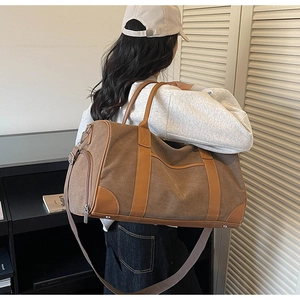 Brown canvas travel bag with leather details shown on model in a lifestyle setting