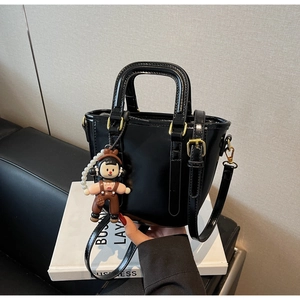 Détail d'un sac seau en cuir verni noir avec charm poupée et chaîne de perles élégante