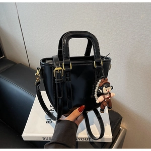 Détail d'un sac seau noir brillant avec finitions dorées et pendentif de fille mignon