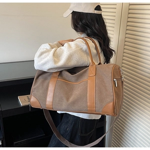 Detail of canvas travel bag featuring brown leather handles and adjustable shoulder strap