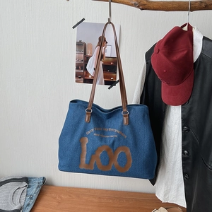 Detail of blue denim tote bag with brown leather handles and artistic letter prints