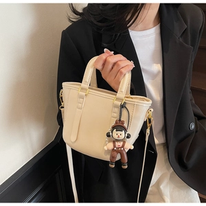 Détail du sac seau en cuir crème avec breloque d'ours et finitions dorées chic