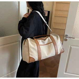 Close-up of cream canvas travel bag with brown leather handles and side zipper pocket