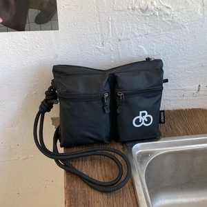 Detail of waterproof black nylon shoulder bag featuring dual zipper pockets and rope strap