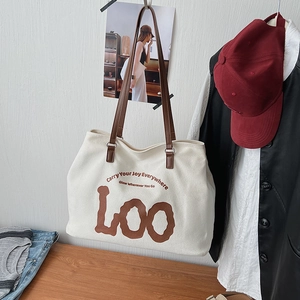 Detail of white canvas tote bag featuring brown leather straps and artistic typography