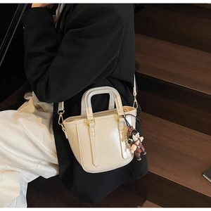 Vue détaillée d'un sac seau blanc crème avec charm de dessin animé sur un escalier